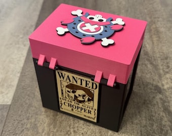 May include: A black and pink box with a pink lid featuring a blue and white skull and crossbones design. The box has a "Wanted" poster with the text "Chopper" on the front.