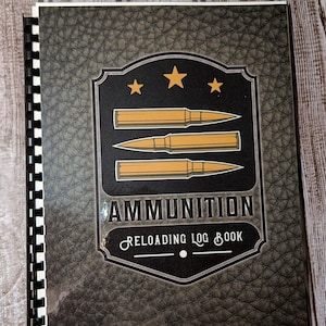 May include: A black and gray leather-bound notebook with a gold logo featuring three bullets and the text "AMMUNITION RELOADING LOG BOOK".