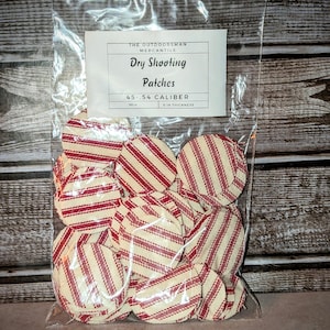 May include: A bag of red and white striped fabric circles labeled "Dry Shooting Patches .45-.54 Caliber 0.18 Thickness" by The Outdoorsman Mercantile.
