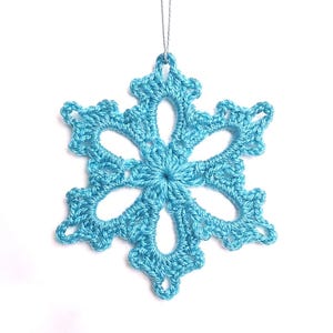 May include: A crocheted snowflake ornament in a light blue color, suspended by a silver string. The snowflake has six symmetrical points with openwork details, perfect for holiday decor.