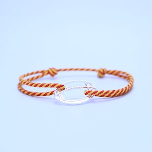 May include: A red and yellow striped cord bracelet with a silver football charm.