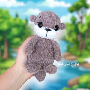 May include: A crocheted plush otter toy with a gray body, white face, and black eyes. The otter is holding its tail in its paws.