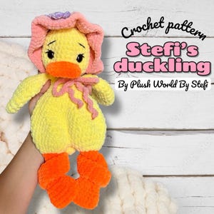 Pode incluir: Um brinquedo de patinho de crochê feito à mão em amarelo, laranja e rosa. O patinho usa um gorro rosa e tem um laço rosa. O texto "Crochet pattern Stefi's duckling By Plush World By Stefi" é visível.