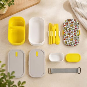 May include: A disassembled lunch box set with a yellow container, white container, gray lids, and a patterned lid. The set includes yellow utensils, a small white container, and a gray strap. The patterned lid features food illustrations.
