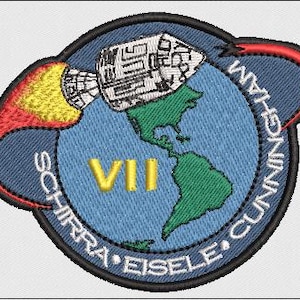 Könnte beinhalten: Gestickter Aufnäher mit blauem Hintergrund, der eine Rakete, die römische Zahl VII und eine Karte der Erde mit grünen Kontinenten zeigt. Die Namen SCHIRRA EISELE CUNNINGHAM sind um den Rand des Aufnähers gestickt.