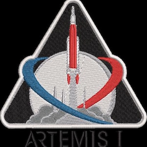 May include: Embroidered patch featuring a rocket launching from a circular platform, with a red and blue arc design. The patch is in a triangular shape with a black background and white border. The text "ARTEMIS I" is at the bottom.