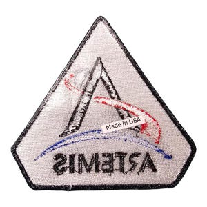 Pu&ograve; includere: Toppa ricamata a forma triangolare con bordo nero. La toppa presenta la parola "ARTEMIS" al contrario, insieme a una "A" stilizzata e tratti rossi e blu. &Egrave; visibile anche la scritta "Made In USA".