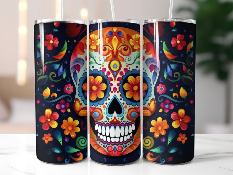 May include: Three stainless steel tumblers with a Day of the Dead sugar skull design. The skull is decorated with colorful flowers and patterns on a black background. Each tumbler has a white straw.