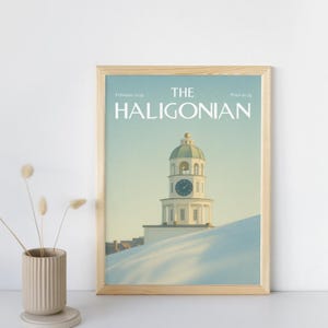 Puede incluir: Una impresión enmarcada de la portada de la revista "The Haligonian". La portada muestra una torre del reloj blanca sobre una colina nevada. El texto incluye "Febrero 2005". El marco es de color marrón claro.