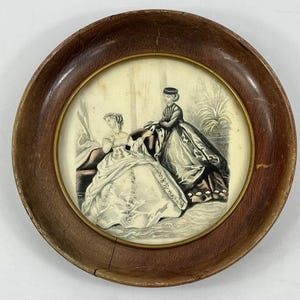 May include: Antique framed print featuring two women in period dresses. The artwork is in a round, wooden frame with a gold inner border. The print depicts a scene with detailed clothing and a classic aesthetic.