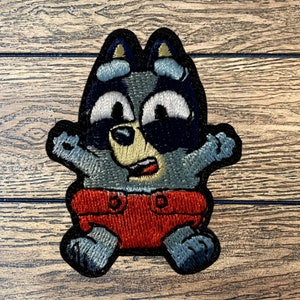 Puede incluir: Parche bordado de un mapache de dibujos animados con un pañal rojo. El mapache tiene una expresión de sorpresa y lleva gafas de sol.