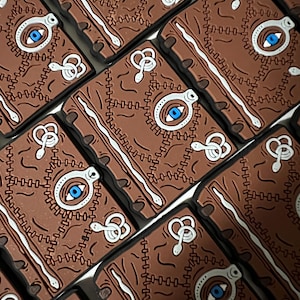 May include: Multiple brown leather-bound books with a white eye and stitching detail. Each book has a white snake design on the cover.