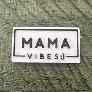 Op de afbeelding: Een roze rechthoekige patch met een zwarte rand en de tekst "MAMA VIBES :)" in zwart.