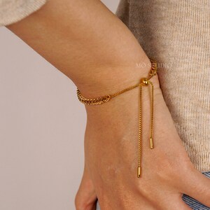 May include: A gold chain bracelet with a sliding knot closure. The bracelet is made of two different chain styles, one thicker and one thinner. The bracelet is adjustable and can be worn at different lengths.