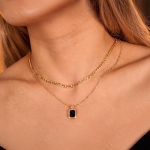 May include: A gold chain necklace with a black square pendant. The necklace is layered with a second, thinner chain.