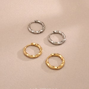 May include: Four hoop earrings in two different sizes. Two are gold and two are silver. The hoops are twisted and have a textured surface.