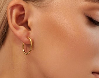 May include: Gold hoop earrings worn in a person's ear. The earrings are simple and classic.