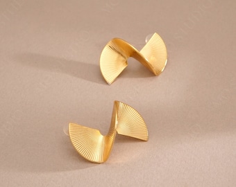 May include: A pair of gold-colored, abstract-shaped earrings. Each earring features a fan-like design that curves and twists, creating a unique, modern look. The earrings are set against a neutral background. The brand name "MŌ STUDIO" is visible at the bottom.
