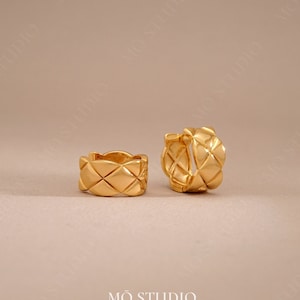 May include: A pair of gold-toned hoop earrings with a quilted design. The earrings are made of metal and have a polished finish.