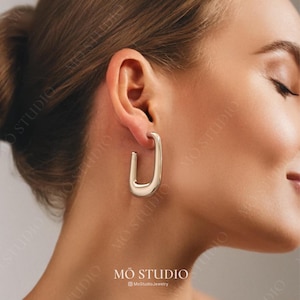 May include: Silver hoop earrings with a unique rectangular shape. The earrings are large and have a smooth, polished finish.