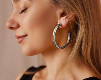 May include: A close-up of a person wearing large, silver hoop earrings. The earrings are thick and have a smooth, polished finish.