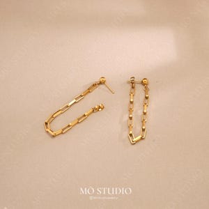 May include: A pair of gold chain earrings with a simple, minimalist design. Each earring features a delicate chain made of small, square-shaped links.
