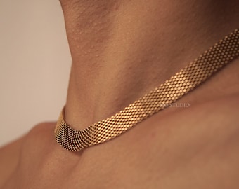 May include: A gold chain necklace with a mesh design. The chain is made of small, round links that are woven together to create a delicate and intricate pattern.