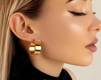 May include: Gold hoop earrings with a thick band. The earrings are worn by a person with their head tilted down. The earrings are a simple and elegant design.