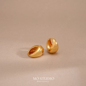 Könnte beinhalten: Ein Paar goldene Creolen. Die Ohrringe sind schlicht und elegant, mit einer glatten, abgerundeten Oberfläche.