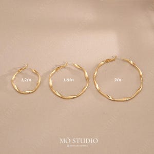 May include: Three gold-coloured hoop earrings of different sizes. The smallest is 3 cm in diameter, the middle one is 4 cm, and the largest is 5 cm. Each earring features a twisted design. The brand name "MŌ STUDIO" is at the bottom.