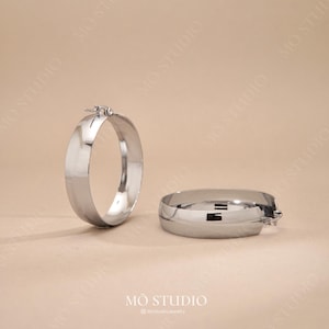 May include: A pair of silver hoop earrings with a smooth, polished finish. The earrings are large and have a slightly curved shape.