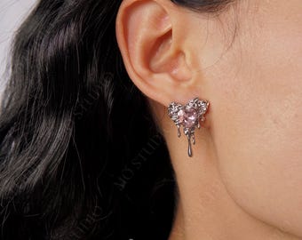 May include: Silver heart-shaped earrings with a pink crystal in the centre. The heart is dripping with silver, creating a melted effect.