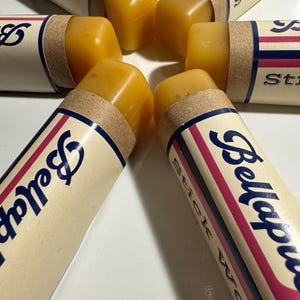 May include: Five stick waxes in brown cardboard tubes with red and blue trim. The tubes are labeled "Bellaps" and "Stick Wax". The waxes are a bright orange color.