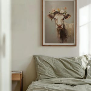 May include: A framed print of a white cow with a flower crown on its head. The cow is looking directly at the viewer. The background is a light blue colour.