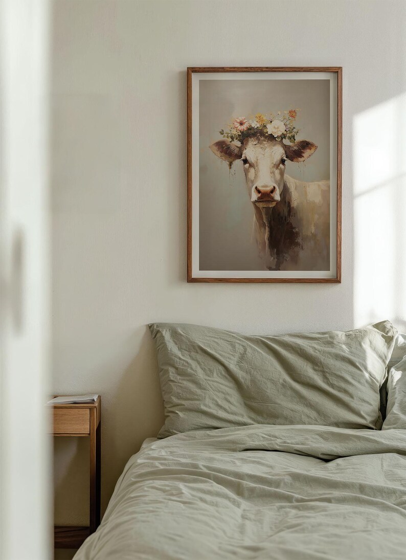 May include: A framed print of a white cow with a flower crown on its head. The cow is looking directly at the viewer. The background is a light blue colour.