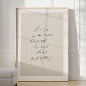 Puede incluir: Un póster beige con marco dorado, que presenta una cita escrita a mano: "Encuentra la alegría en las cosas simples y la vida siempre será plena."