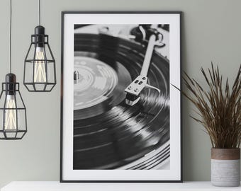May include: Black and white photograph of a record player with a vinyl record spinning on the turntable. The needle is visible on the record.