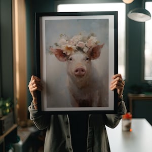 Puede incluir: Una pintura enmarcada de un cerdo con una corona de flores. El cerdo es blanco con orejas rosadas y un hocico rosado. Las flores son blancas, rosas y amarillas. El fondo es azul claro.