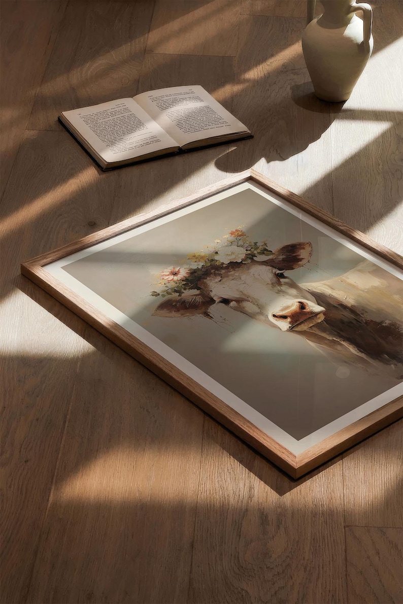 May include: A framed print of a cow wearing a flower crown. The cow is white with brown patches and has a gentle expression. The background is a soft, muted grey.