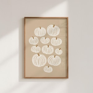 Op de afbeelding: Een ingelijste kunstdruk met witte pompoenen met bruine stelen op een beige achtergrond. De pompoenen variëren in grootte en zijn in een patroon gerangschikt. Het kunstwerk is ingelijst in een houten frame.