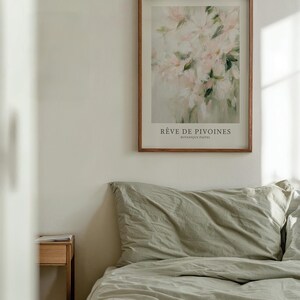 May include: A framed art print featuring a watercolor painting of pink flowers with green leaves. The print is titled "R&ecirc;ve de Pivoines" and is displayed above a bed with sage green bedding. A small wooden nightstand is visible.