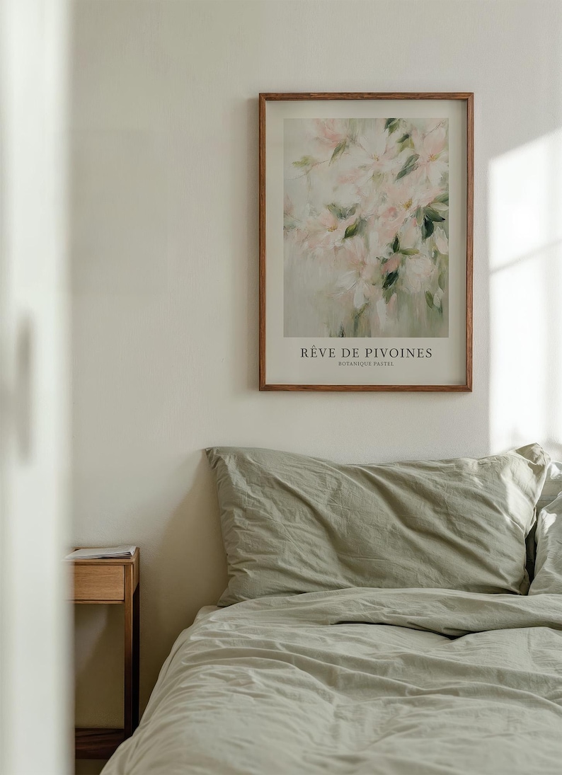 May include: A framed art print featuring a watercolor painting of pink flowers with green leaves. The print is titled "R&ecirc;ve de Pivoines" and is displayed above a bed with sage green bedding. A small wooden nightstand is visible.