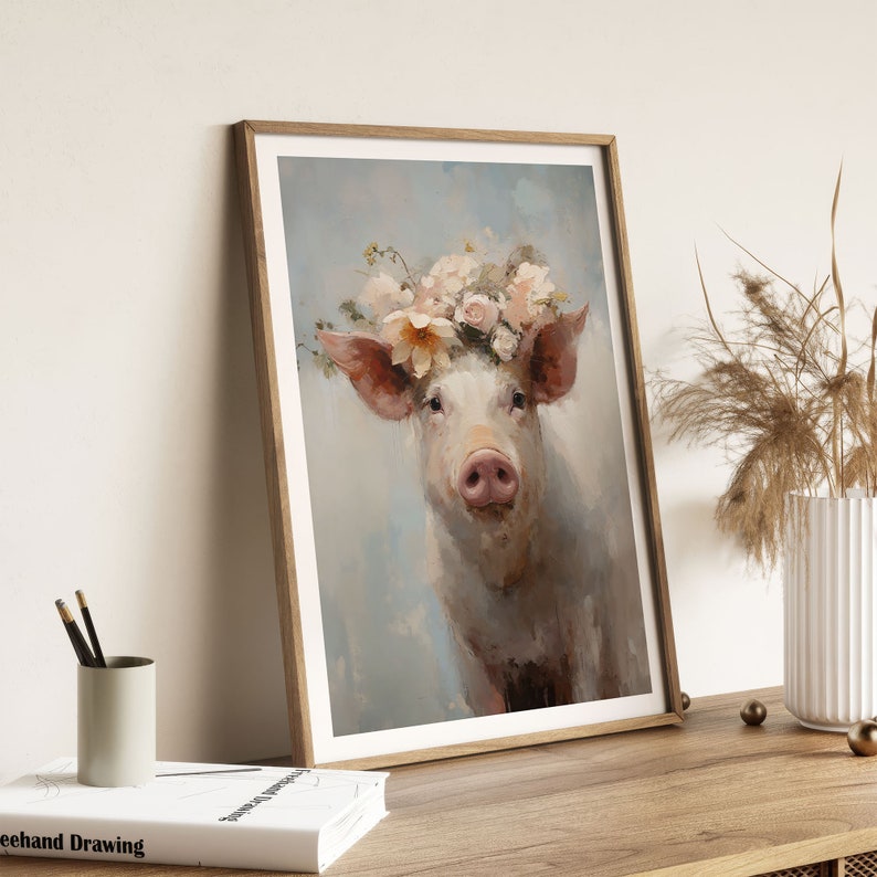 Puede incluir: Una pintura enmarcada de un cerdo con una corona de flores rosas y blancas. El cerdo mira directamente al espectador con una expresi&oacute;n suave. El fondo es de un azul suave.
