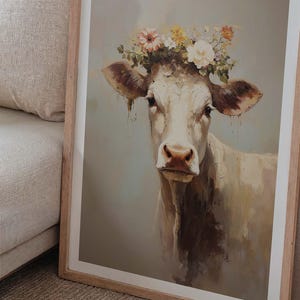 May include: A framed painting of a white cow wearing a flower crown. The cow is looking directly at the viewer with a soft, gentle expression. The background is a light blue-grey colour.