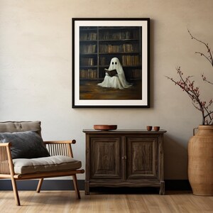 May include: A framed painting of a white ghost sitting in a library reading a book. The ghost is wearing a white gown and has a faint outline of a face. The library is filled with bookshelves and books.