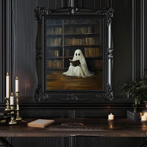 May include: A black framed painting of a white ghost reading a book in a library. The ghost is sitting on the floor in front of a bookshelf filled with books. The painting is hanging on a black wall with candles and a wooden table in front of it.