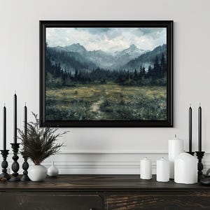 K&ouml;nnte beinhalten: Ein gerahmtes Landschaftsbild mit einer Bergkette und einem Wald im Vordergrund. Das Bild ist in einem schwarzen Rahmen und h&auml;ngt an einer wei&szlig;en Wand. Vor dem Bild stehen Kerzen und eine Pflanze auf einem dunklen Holztisch.