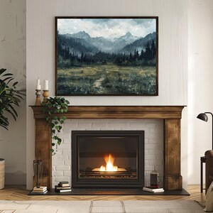 K&ouml;nnte beinhalten: Ein Kamin mit einem Holzmantel und einem Backsteinsockel. Der Kamin hat einen schwarzen Metallfeuerraum mit einer Glast&uuml;r und ein Feuer, das darin brennt. &Uuml;ber dem Kamin h&auml;ngt ein gerahmtes Landschaftsbild mit einer Bergszene.