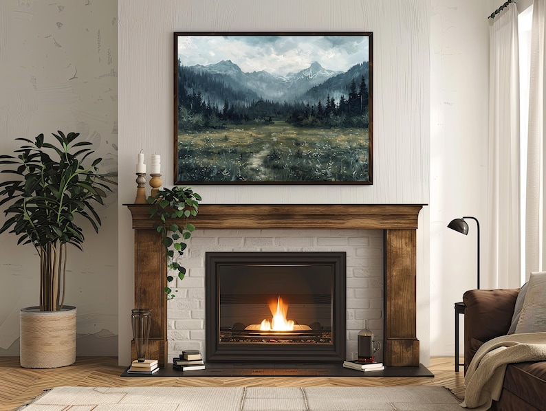 K&ouml;nnte beinhalten: Ein Kamin mit einem Holzmantel und einem Backsteinsockel. Der Kamin hat einen schwarzen Metallfeuerraum mit einer Glast&uuml;r und ein Feuer, das darin brennt. &Uuml;ber dem Kamin h&auml;ngt ein gerahmtes Landschaftsbild mit einer Bergszene.