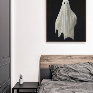 Peut inclure: Une peinture encadr&eacute;e repr&eacute;sentant un fant&ocirc;me blanc avec deux yeux noirs est accroch&eacute;e &agrave; un mur blanc au-dessus d'un lit avec une housse de couette ray&eacute;e gris et blanc.
